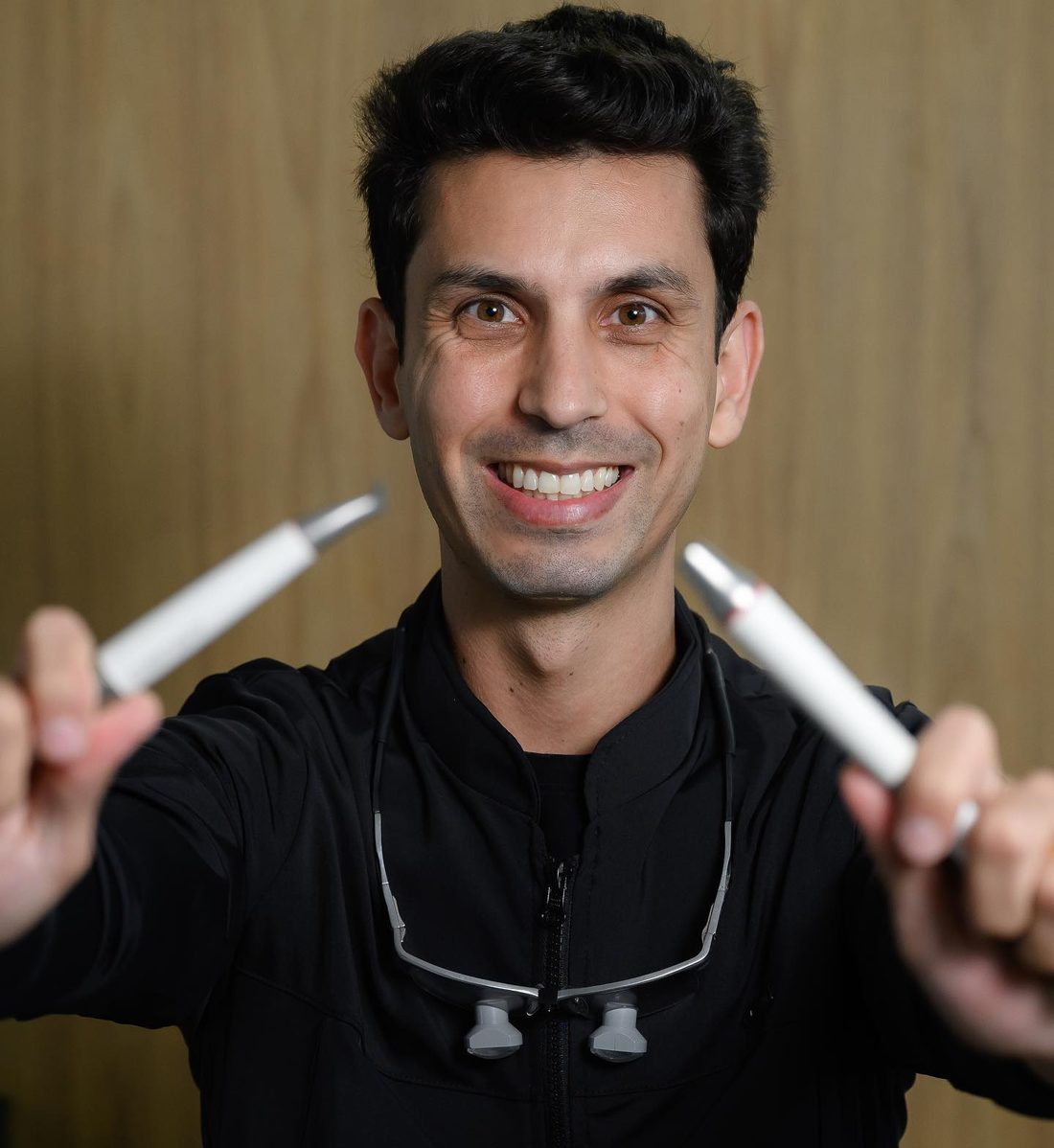 Dr. Felipe Giani sorrindo com instrumentos odontológicos nas mãos