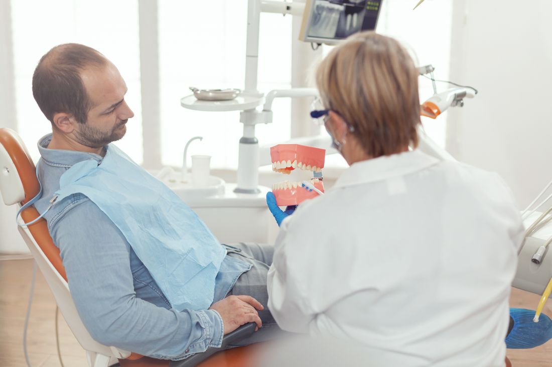 Dentista mostrando modelo de arcada dentária ao paciente